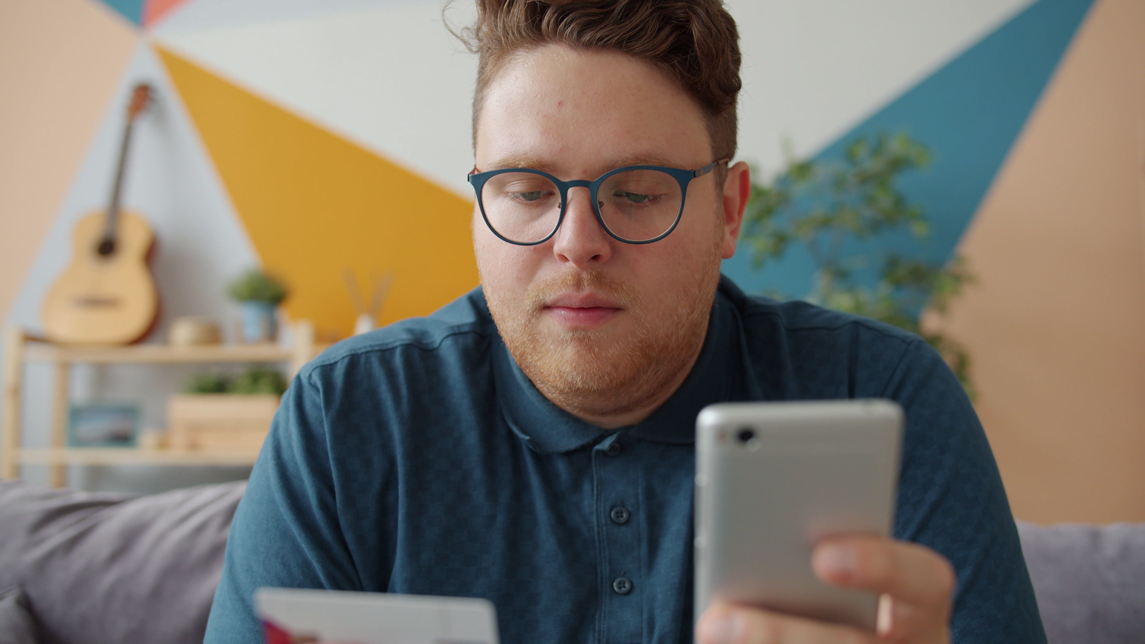 Man using a smartphone and credit card for online payments in a modern living room