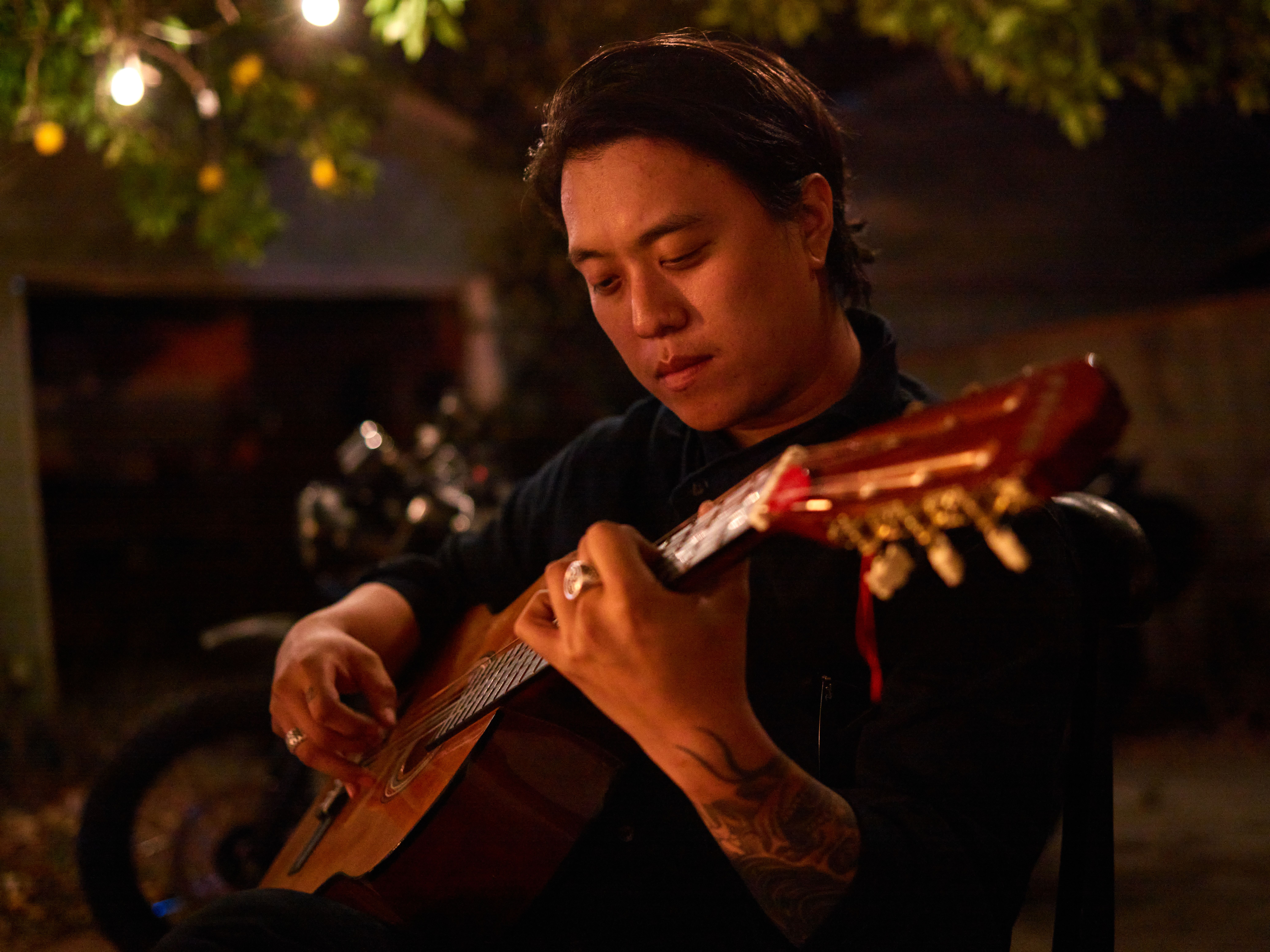 Musician playing acoustic guitar under warm lights in a cozy outdoor setting