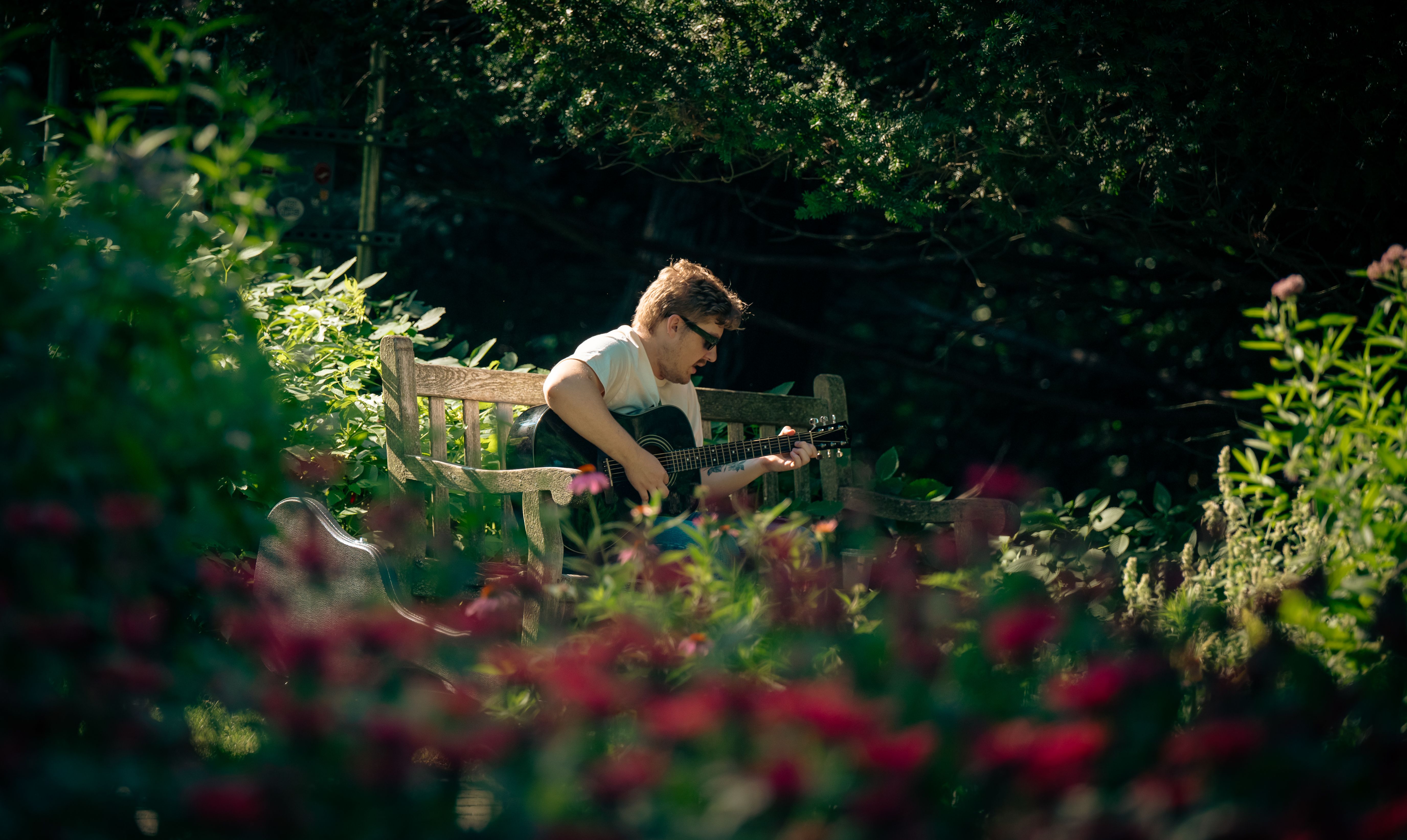 Musician playing acoustic guitar on a garden bench surrounded by greenery
