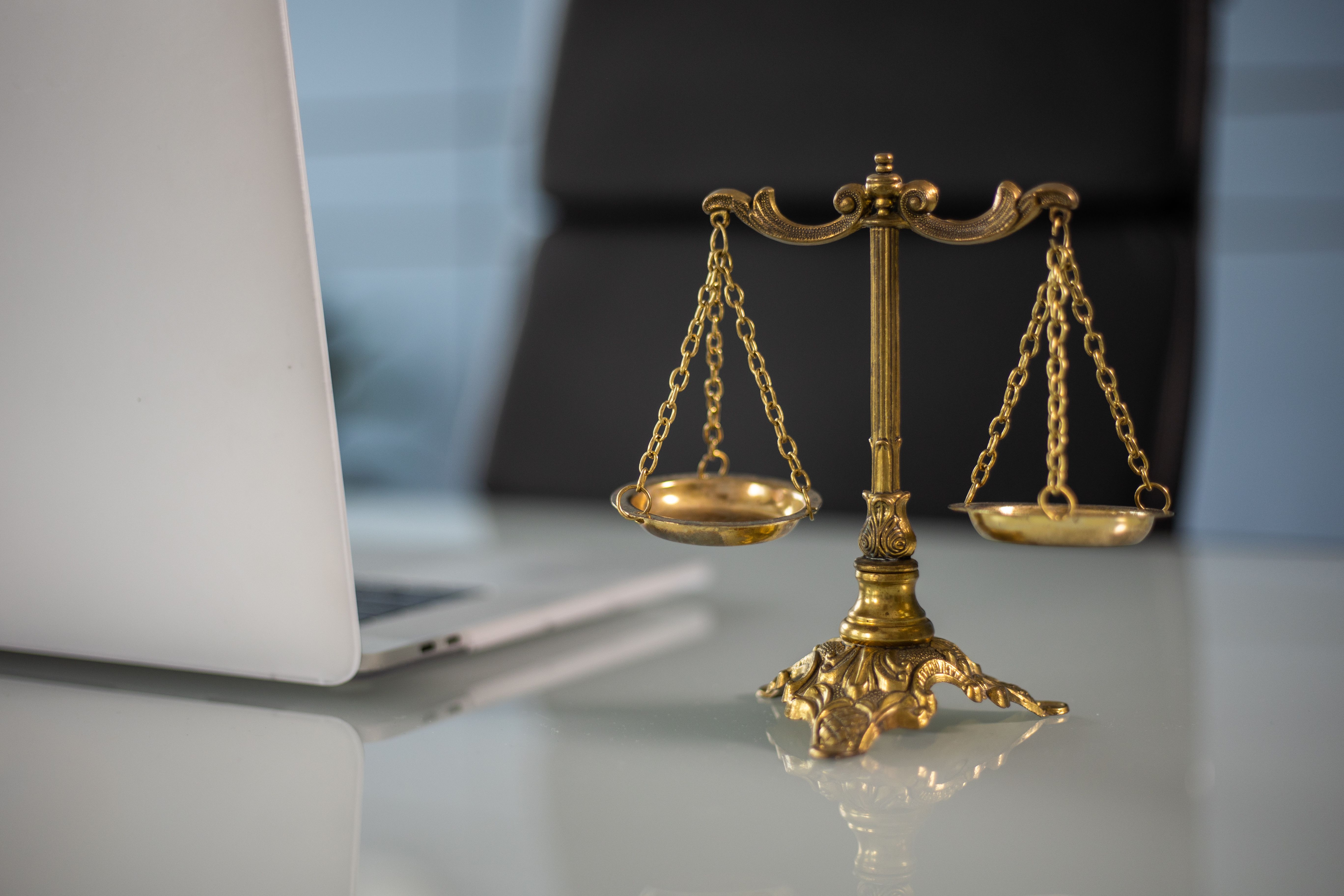 Golden justice scales beside a laptop, symbolizing balance in legal and financial decisions